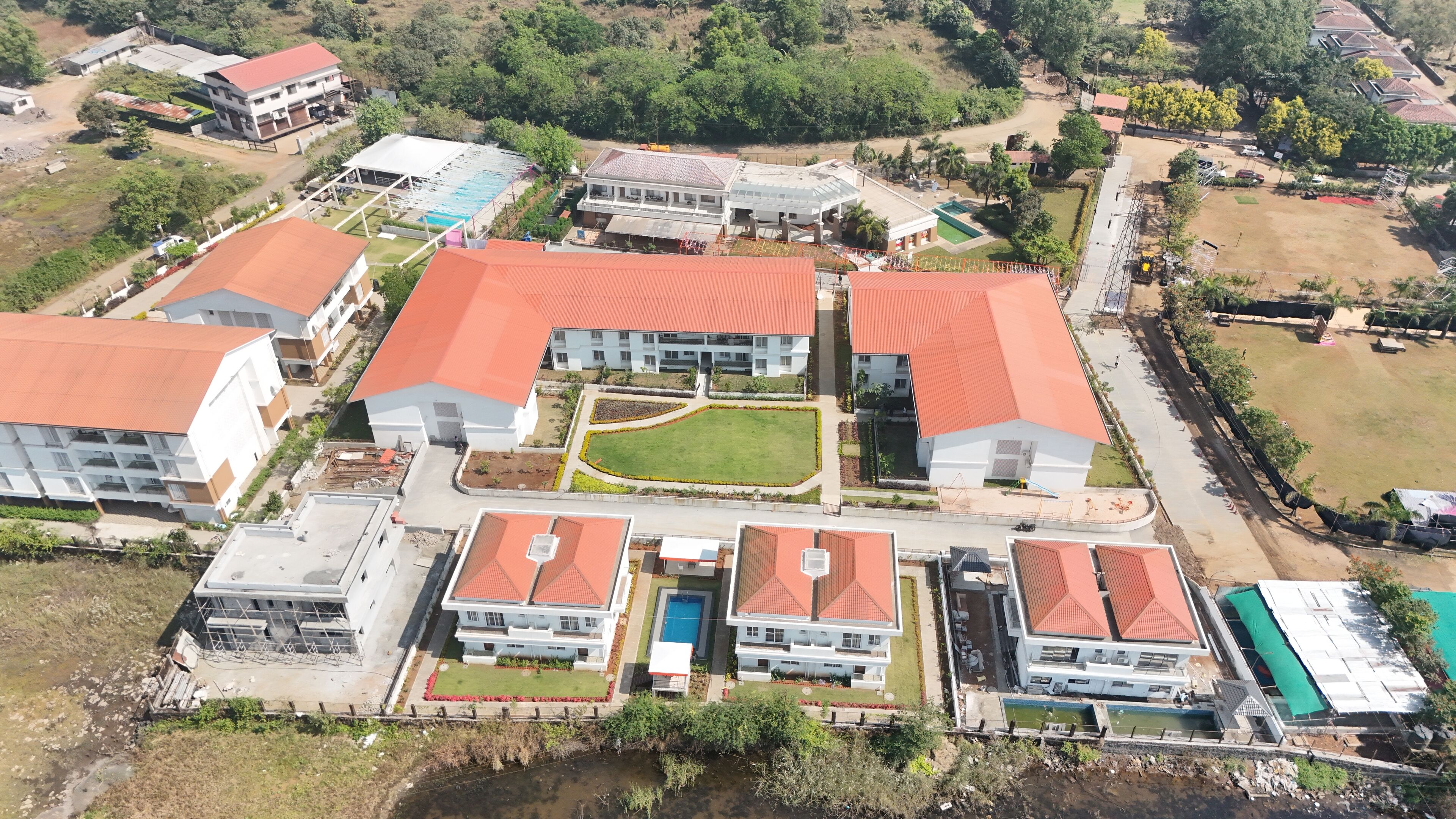 An aerial view of a residential area with multiple buildings, including houses and apartment complexes, with red-tiled roofs and green lawns.