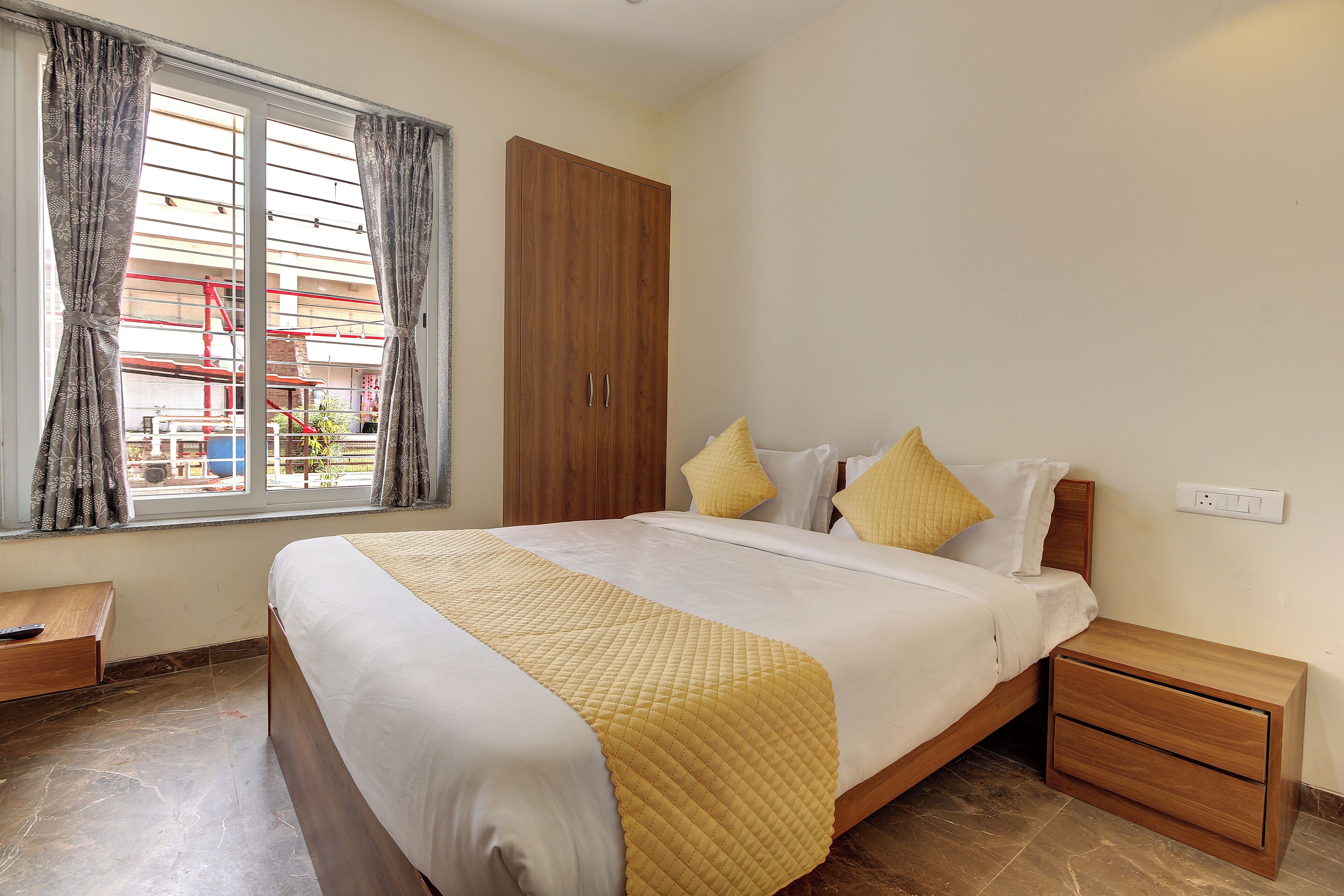 A neatly made bed with a yellow quilt, wooden nightstands, a wardrobe, and a window with curtains.