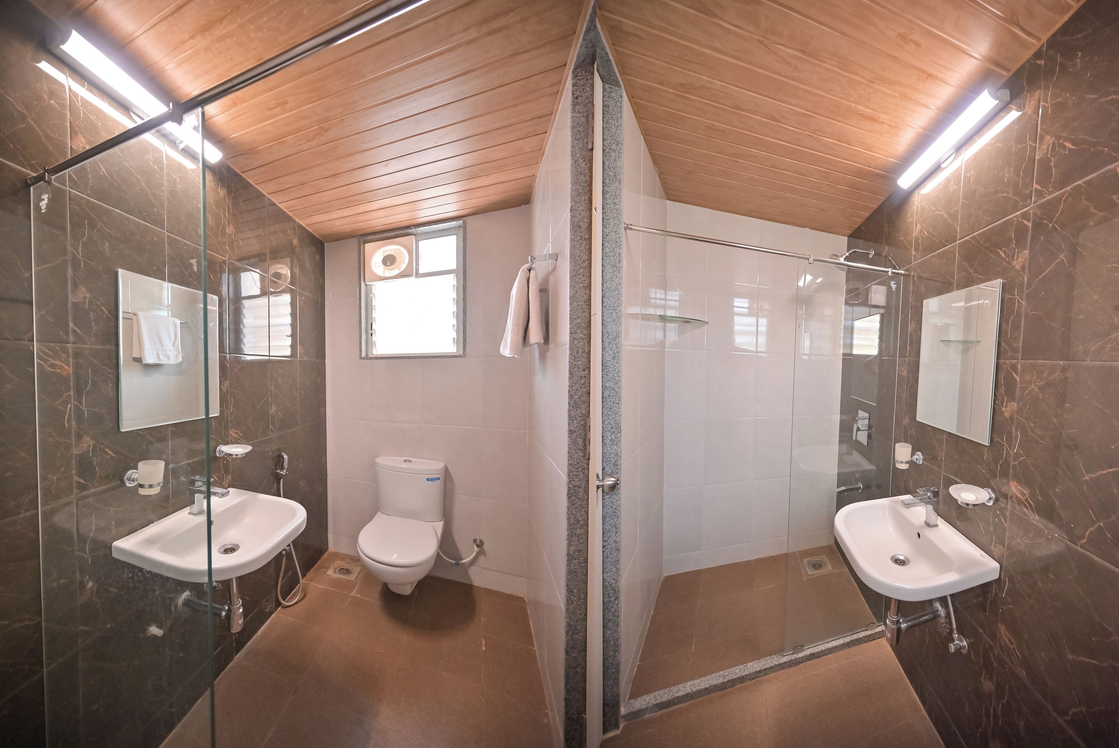 Et moderne badeværelse med to håndvaske, toilet og brusekabine med glasvægge.