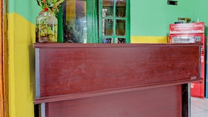 A reception desk with a wooden top and a lower compartment, a green door, and a Coca-Cola refrigerator.