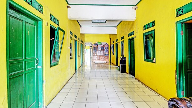 A corridor with yellow walls and green doors, leading to a room with a bed and a window.