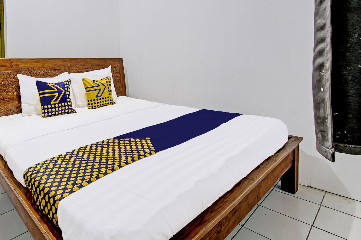 A bed with a wooden headboard, white bedding, and two decorative pillows with a yellow and blue pattern.