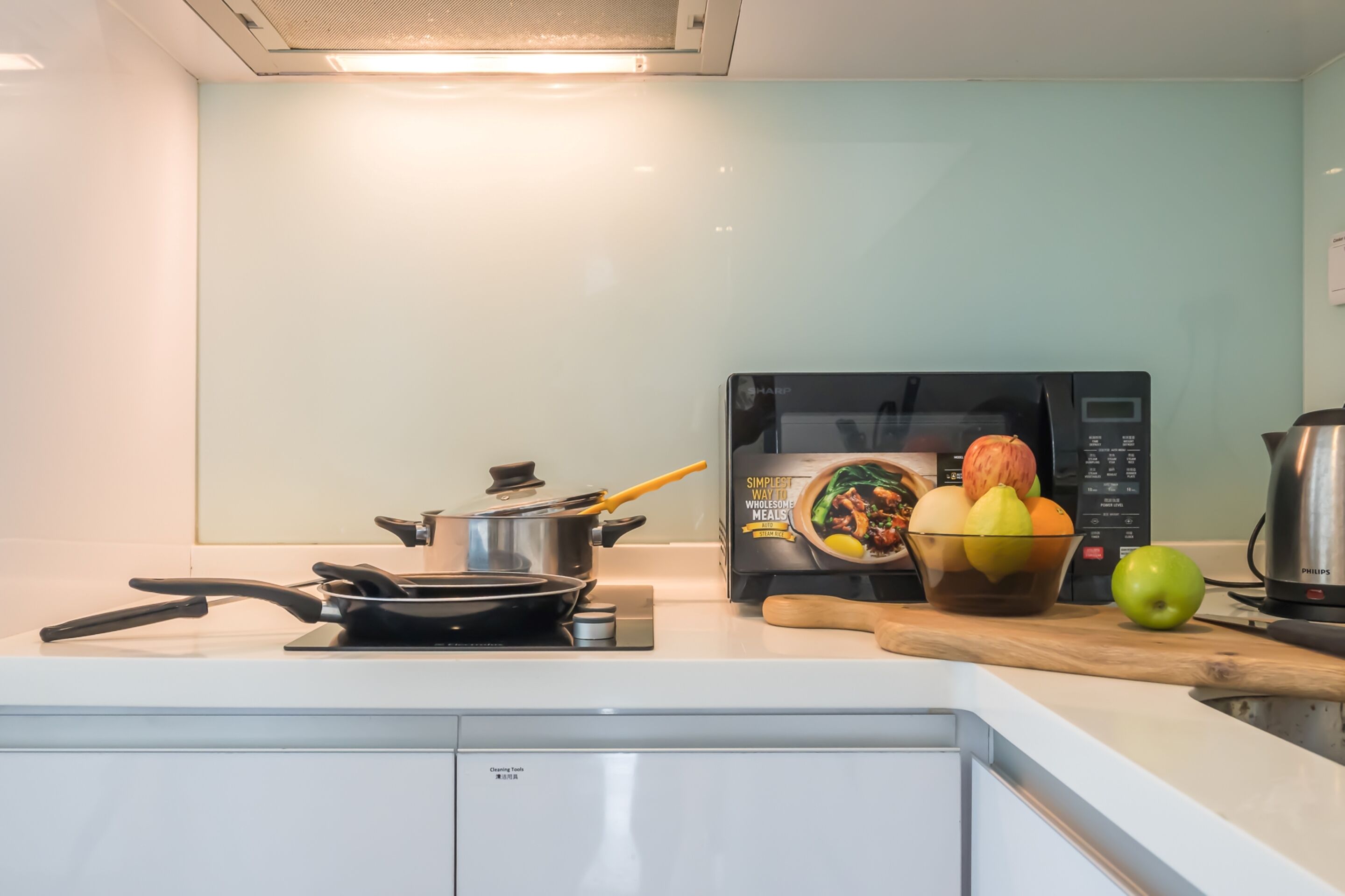 Een moderne keuken met een magnetron, een koekenpan, een pan, een fruitschaal en een waterkoker.