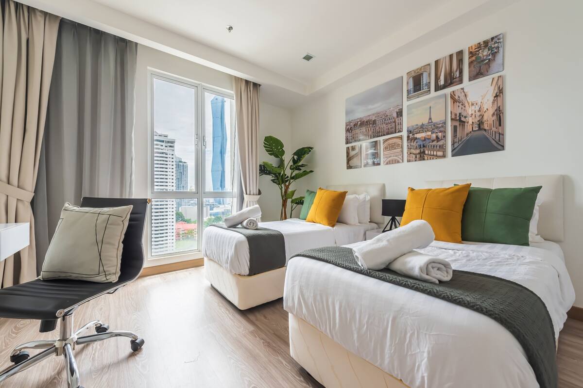 Een hotelkamer met twee bedden, een bureau, een stoel en een groot raam met uitzicht op de stad.
