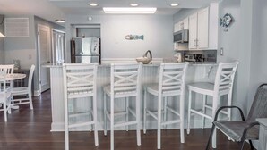 Una cocina con muebles blancos, una isla central con taburetes y un adorno de pared con motivos marinos.