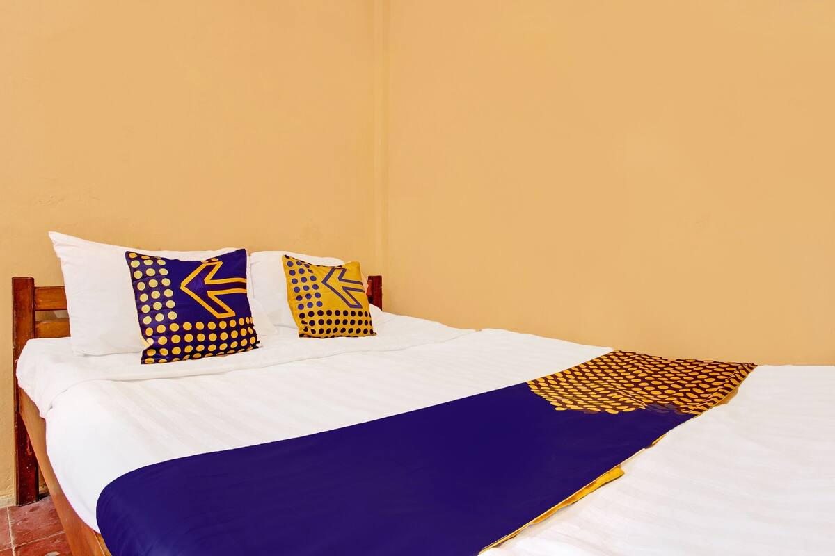 A bed with white sheets, two pillows with yellow and blue patterns, and a blue blanket.