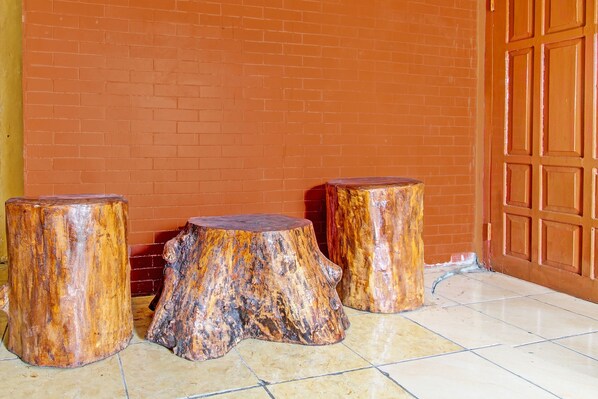 Three wooden stools with a natural finish, placed on a tiled floor against a brick wall and a wooden door.