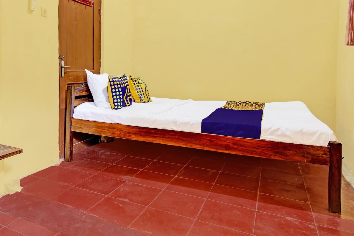 A single bed with a wooden frame, white bedding, and patterned pillows.