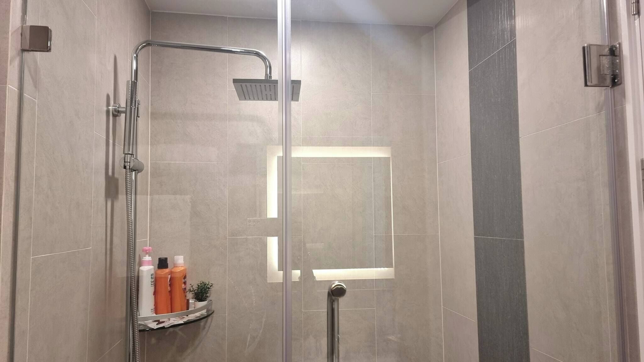 Un moderno box de ducha con puerta de cristal, cabezal de ducha de mano y panel de control en la pared.