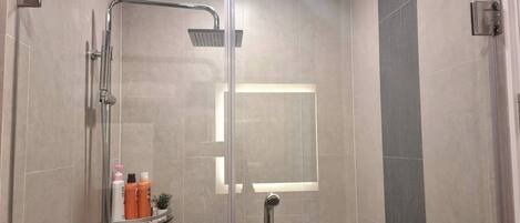 Un moderno box de ducha con puerta de cristal, cabezal de ducha de mano y panel de control en la pared.