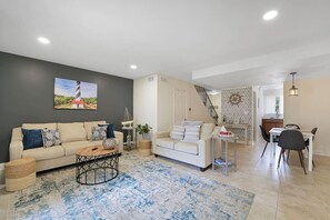 Relax in this inviting living room with a beige sofa, wooden coffee table, and a beautiful painting of a lighthouse.