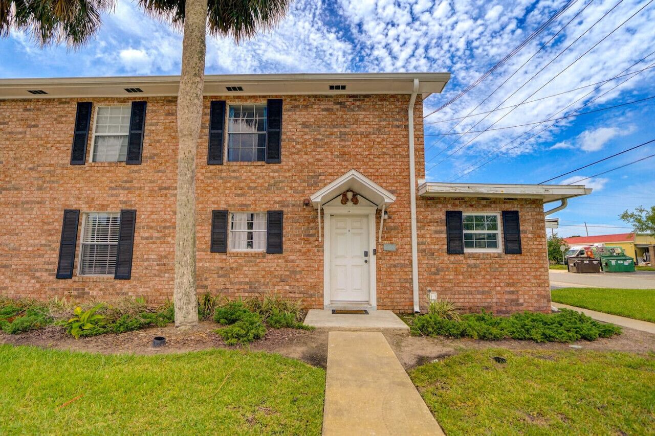 A two-story brick building with a white front door, black shutters, and a small porch.