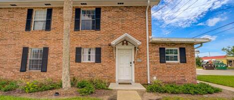 A two-story brick building with a white front door, black shutters, and a small porch.