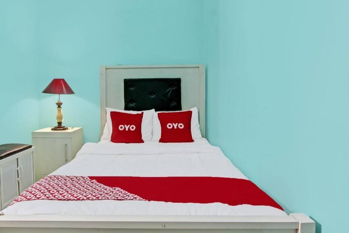 A bed with two pillows, a bedside lamp, and a red throw blanket.