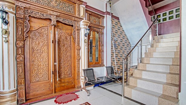 Una escalera con barandilla de metal, una puerta de madera con detalles tallados y una alfombra estampada en el suelo.