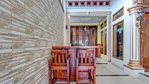 Un pasillo con un banco y sillas de madera, piso de baldosas y un muro decorativo.