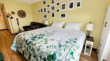 Une chambre à coucher avec un lit, une table de chevet, une lampe, un mur orné de tableaux encadrés et une porte.
