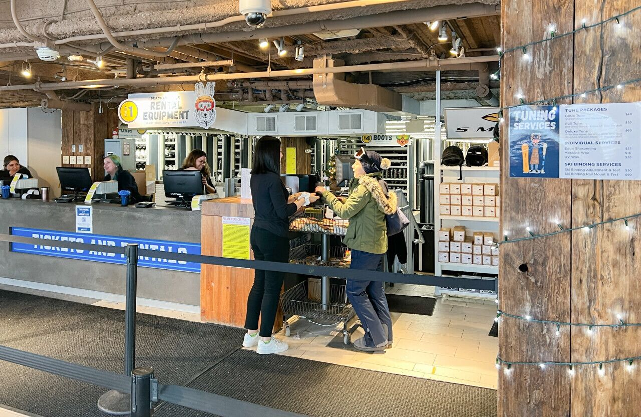 Mostrador de alquiler de equipo con un cartel de servicios de alquiler, una estación de computadoras y una exhibición de equipamiento para esquiar.