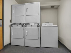 A laundry room with four stacked washers and dryers, a door, and a light switch on the wall.