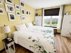 A bedroom with a bed, bedside table, lamp, wardrobe, and a window with a view.