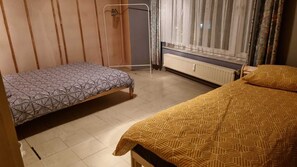 Una habitación con dos camas, un radiador, una ventana con cortinas y un armario de madera.