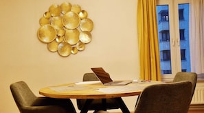 A round wooden table with four chairs, a laptop, and a decorative wall piece.