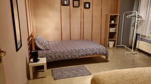 A bedroom with a bed, a nightstand, a radiator, a shelf with a plant, and a window with curtains.