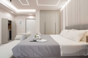 Une chambre d’hôtel moderne avec un lit bien fait, une armoire et une salle de bain visible au fond.