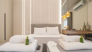 Une chambre d’hôtel moderne avec un lit, deux serviettes blanches, une bouteille et des chaussons.