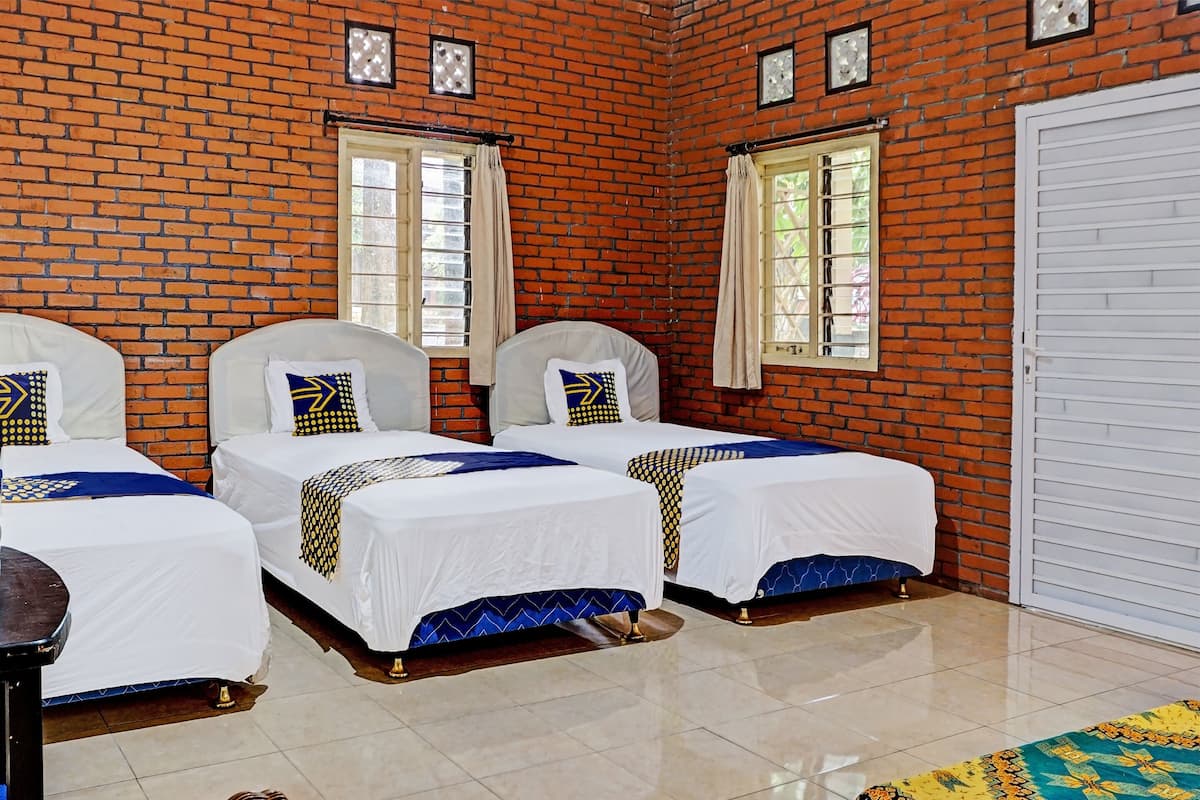 A room with three beds, each with a white bedspread and blue accents, against a brick wall with windows.