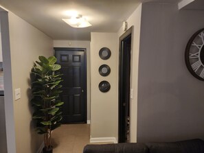 A hallway with a black door, a potted plant, and three wall-mounted clocks. - Beautiful two bedroom. With Wash and Fold services included for Free!!!! (Brooklyn)