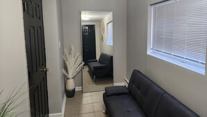 Ein Flur mit einer dunklen Tür, einem Blumentopf, einem Sofa und einem Fenster mit Jalousien.