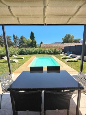 En overdækket terrasse med en pool, to liggestole og et bord.
