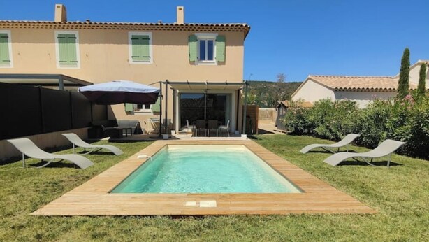 Une piscine rectangulaire avec une terrasse en bois, entourée de pelouse. Il y a deux chaises longues de chaque côté de la piscine.