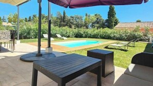 Un espace extérieur aménagé avec une terrasse, une piscine, une table et des fauteuils confortables.
