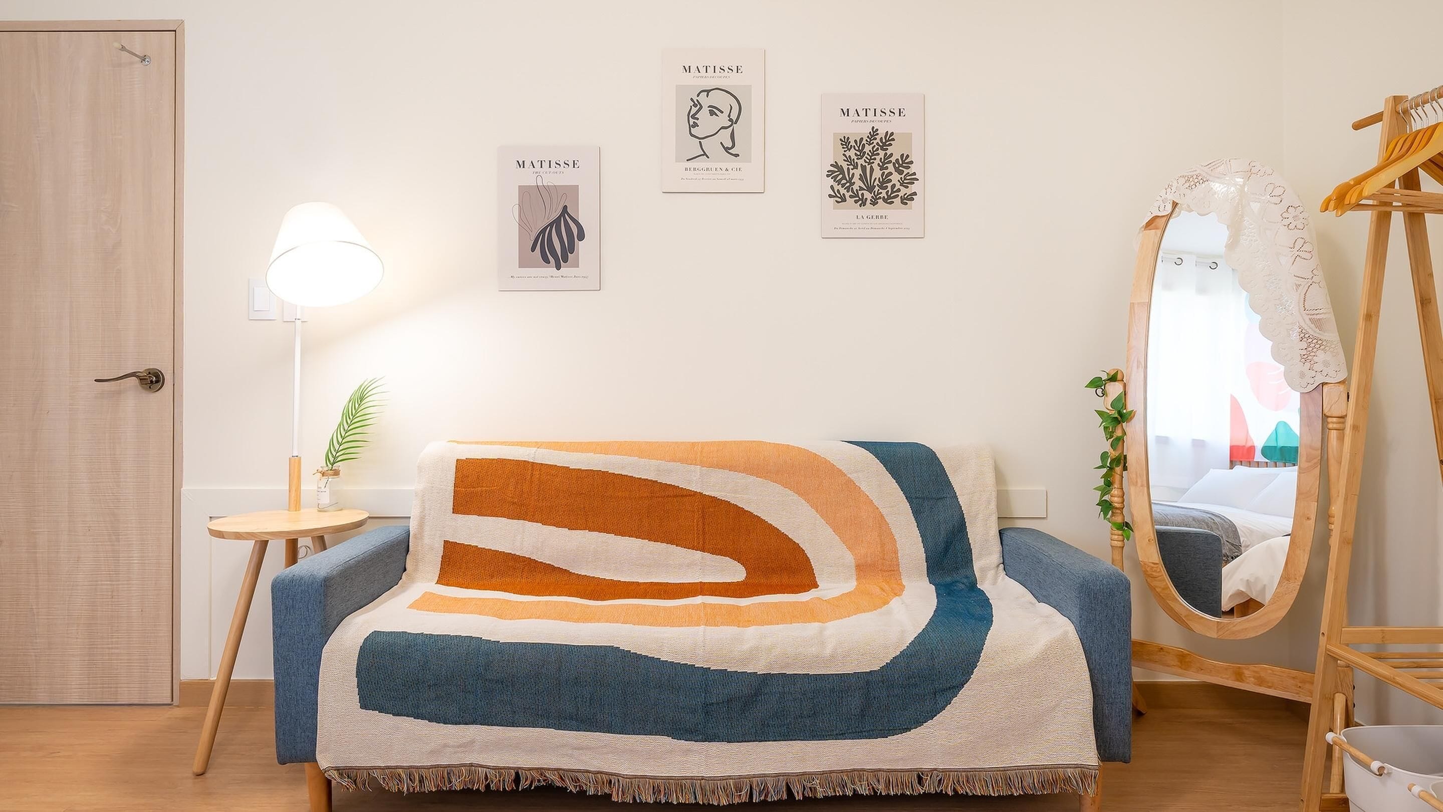 Una habitación con un sofá, una lámpara, un espejo y tres cuadros en la pared.