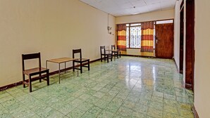 Une pièce avec un sol carrelé, des chaises en bois, une petite table, une fenêtre avec des rideaux à motifs et une porte.