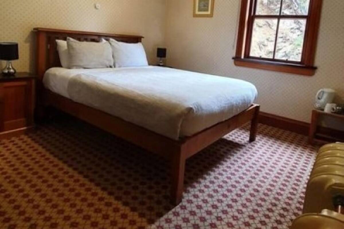 A bedroom with a wooden bed, a nightstand, a window with a view, and patterned carpet.