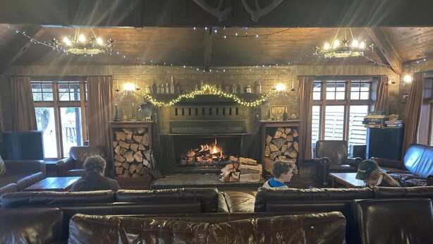 A cozy lounge area with leather sofas, a fireplace, and a stone wall. - Danseys Pass Hotel (Kyeburn Diggings)