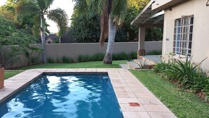 Une piscine rectangulaire dont les bords sont recouverts de carreaux, entourée d’une pelouse bien entretenue et de diverses plantes.