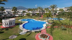 Et resort med en stor, buet swimmingpool omgivet af palmer og en bjergkæde i baggrunden.