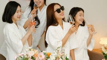 A group of people in white robes at a table with a floral arrangement, a bottle, and a plate of food.