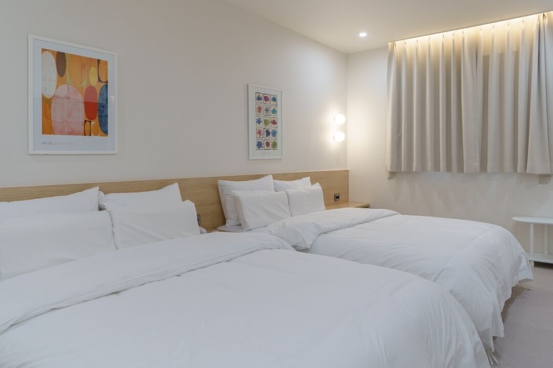 A hotel room with two beds, a wooden headboard, a wall-mounted light, and a window with curtains.