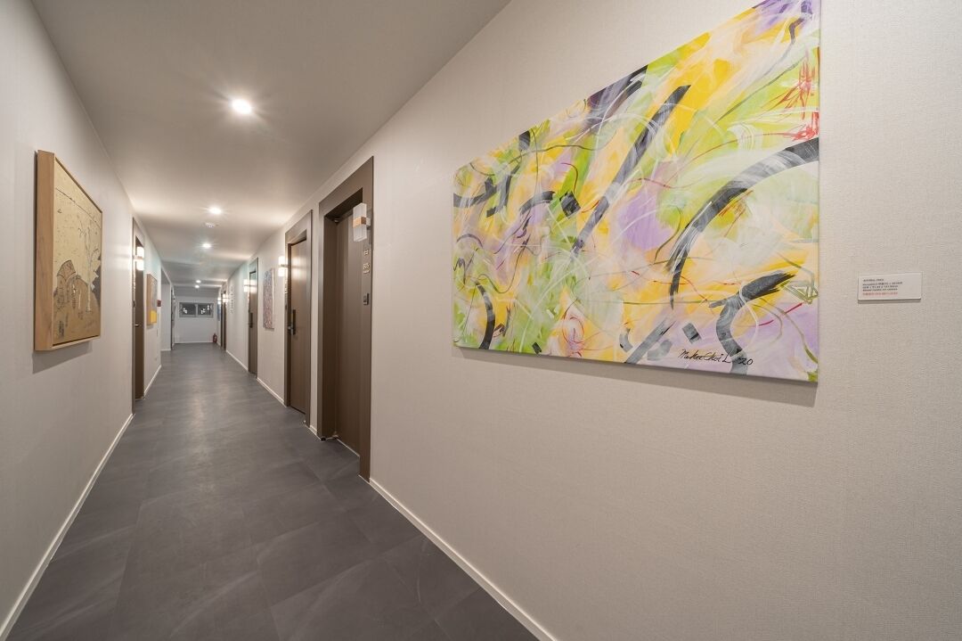 Un pasillo con una obra de arte moderno en la pared derecha, un cuadro enmarcado a la izquierda y una puerta al final.