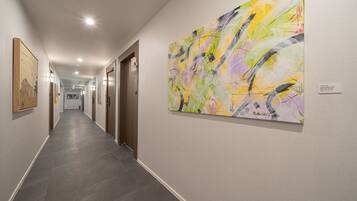 Un pasillo con una obra de arte moderno en la pared derecha, un cuadro enmarcado a la izquierda y una puerta al final.