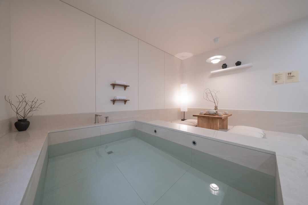 A modern bathroom with a glass-enclosed pool, minimalist design, and a small wooden vanity with a lamp.
