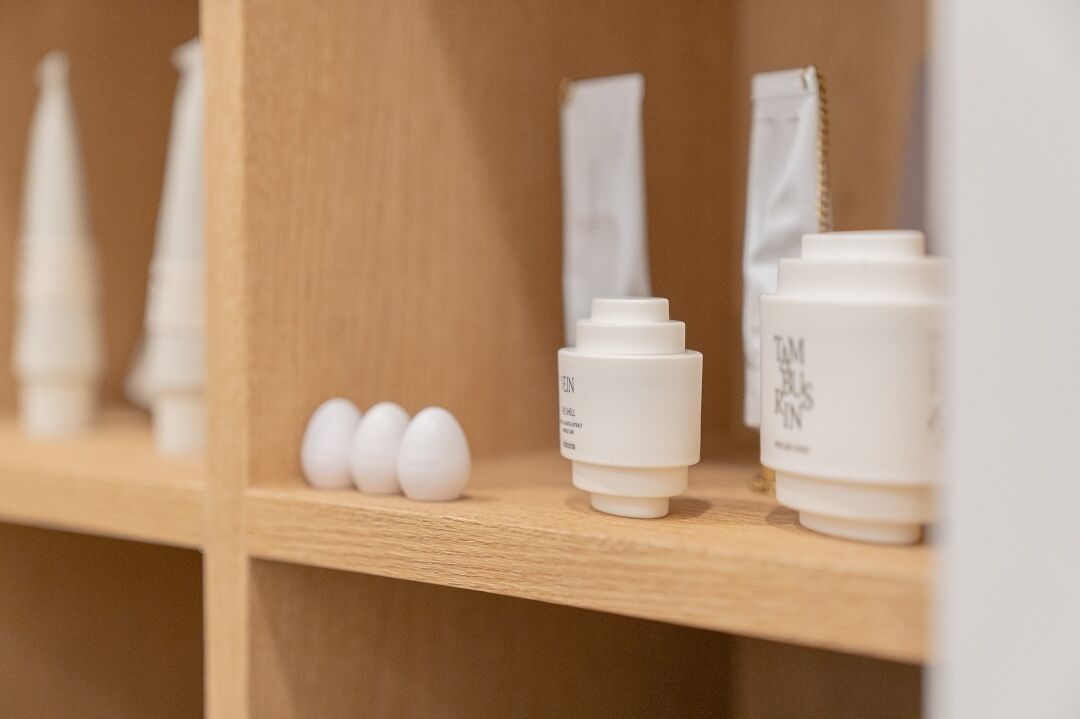 Una estantería con productos para el cuidado de la piel, como tubos y tarros, y tres huevos.