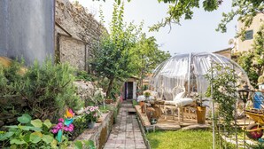 Un giardino con un vialetto che conduce a una serra, circondato da piante e mobili da esterno.
