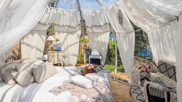 Una tenda allestita con un letto, cuscini, un tavolo con una lampada e una sedia.