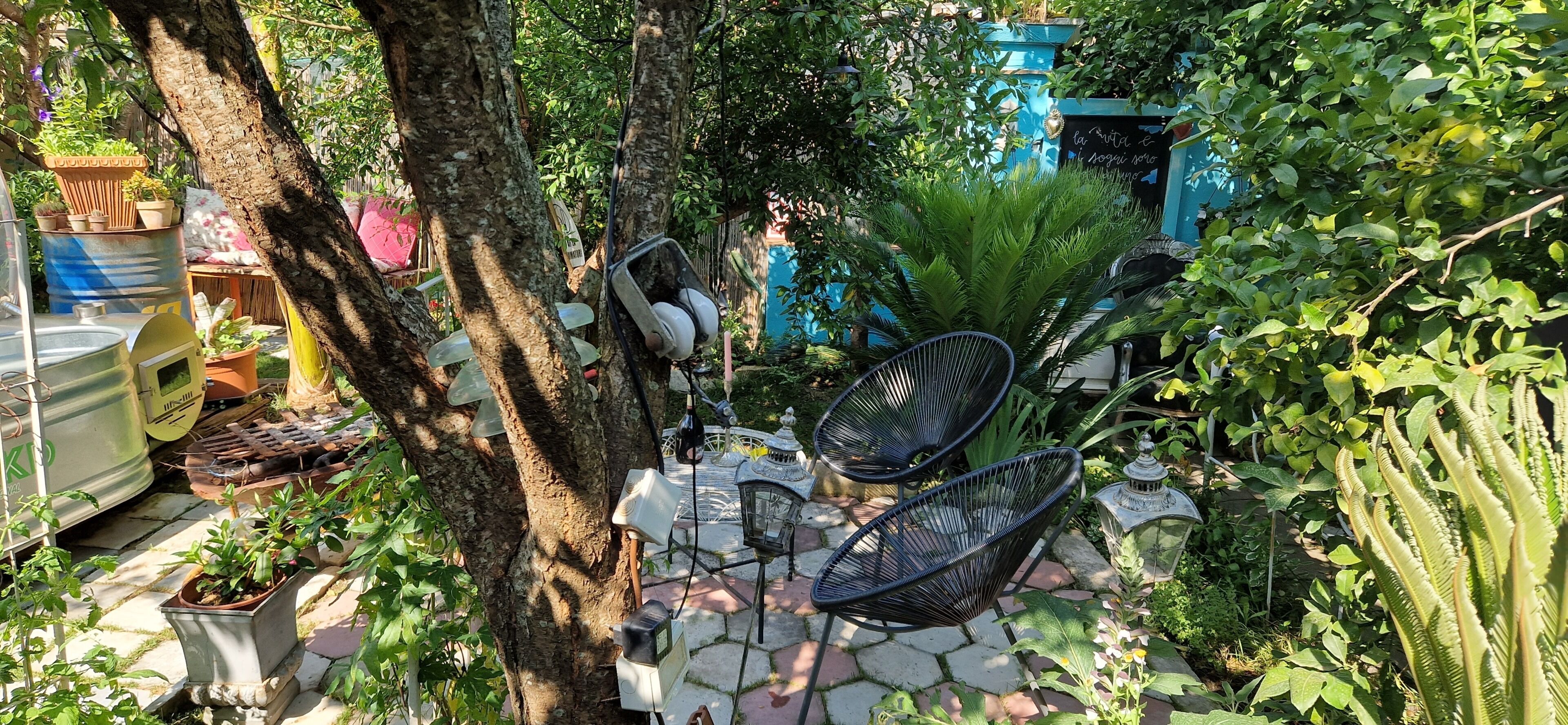 A garden area with outdoor seating, potted plants, and a blue structure in the background.